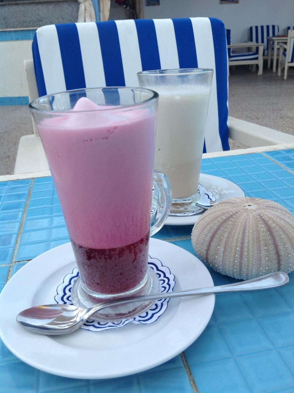 Una mesa con dos vasos de batido, una concha decorativa y una cuchara sobre un plato.