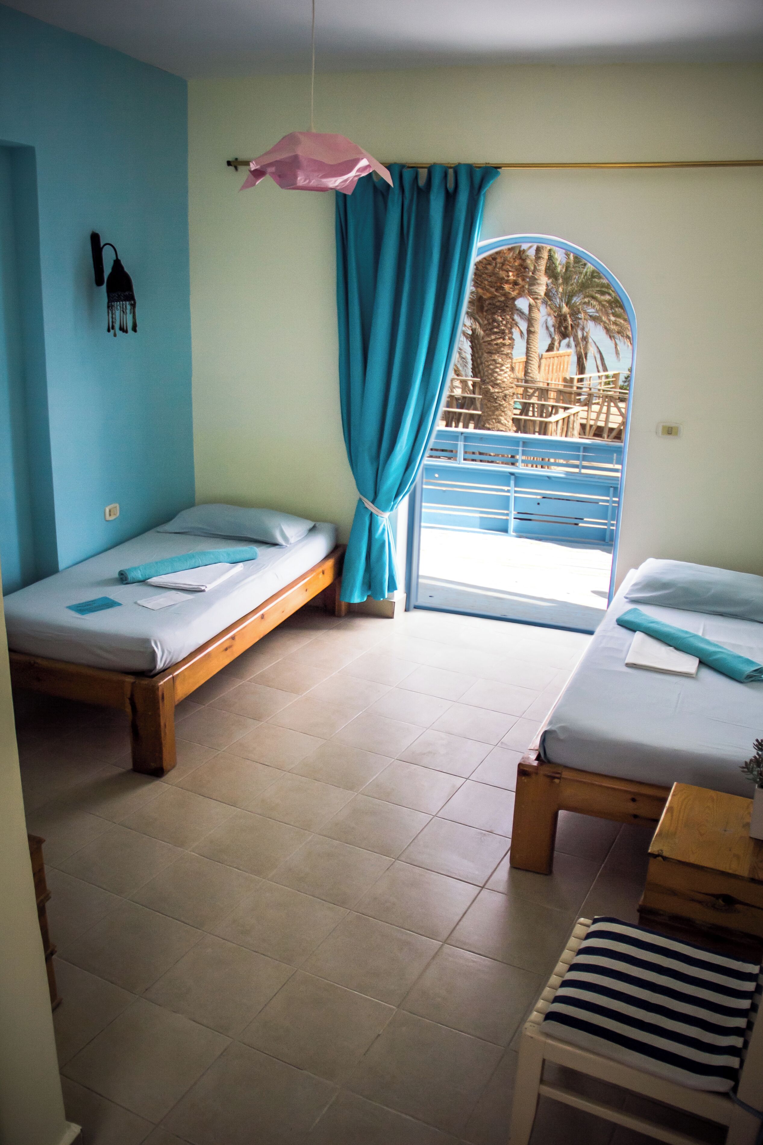 A room with two wooden beds, a small table, and a window with blue curtains.
