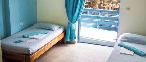 A room with two wooden beds, a small table, and a window with blue curtains.