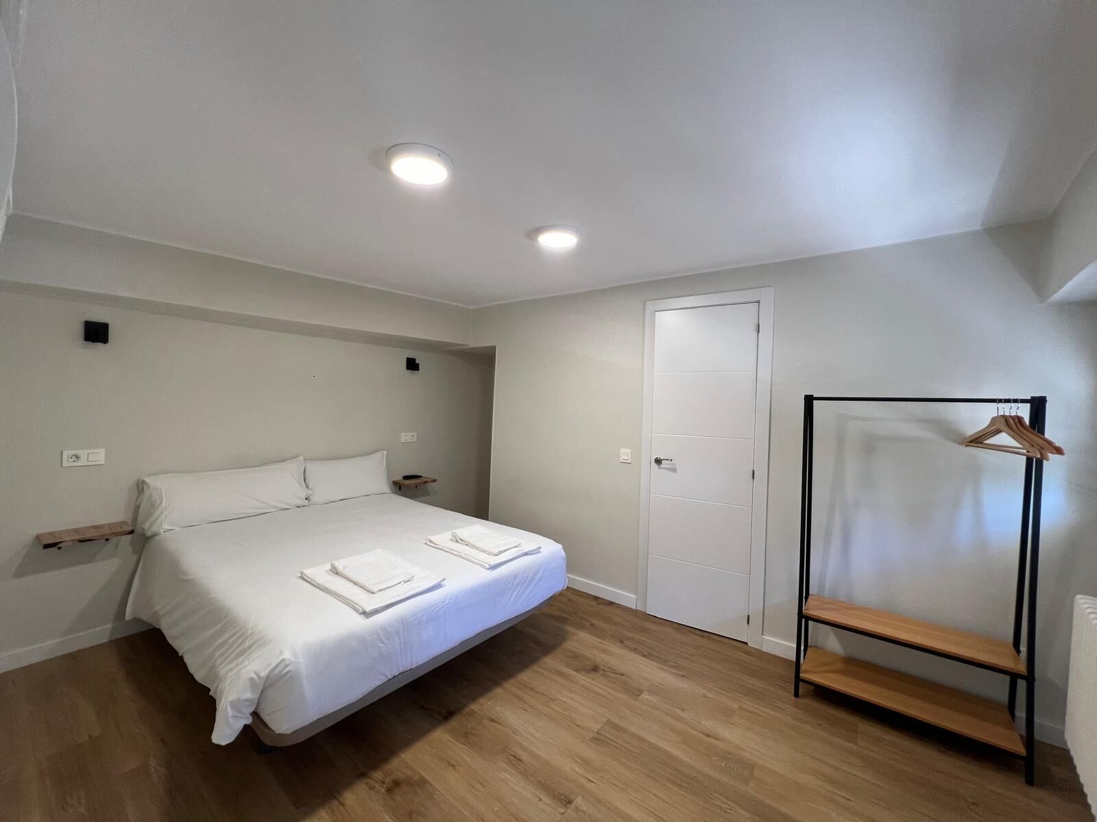 Un dormitorio con cama, suelo de madera, puerta blanca y perchero.