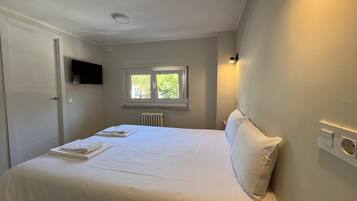 Una camera d'albergo con un letto, una TV a parete, una finestra e un termosifone.