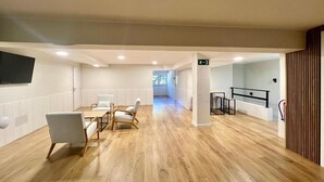 Una habitación amplia con piso de madera, un rincón de descanso con sillas, una mesita y vistas a un balcón.