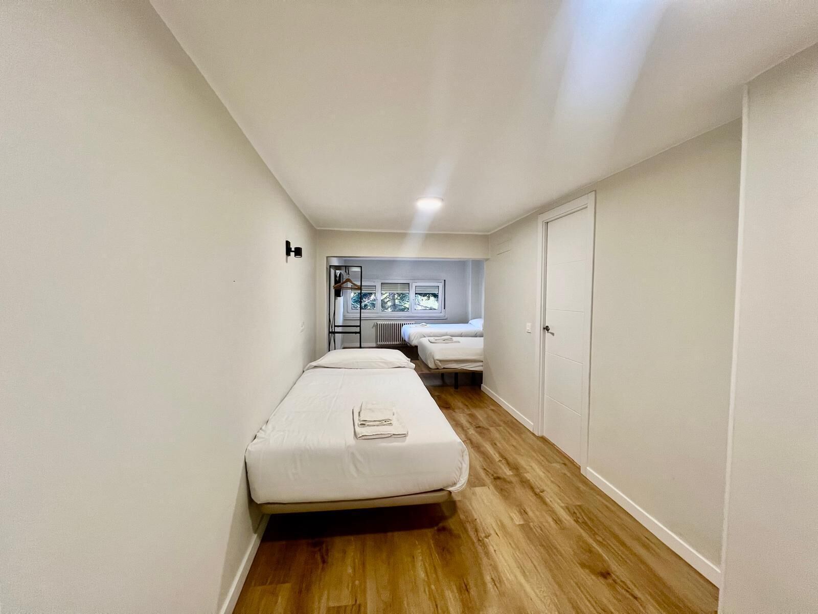 A narrow hallway with a single bed, a radiator, and a window with a view of trees.