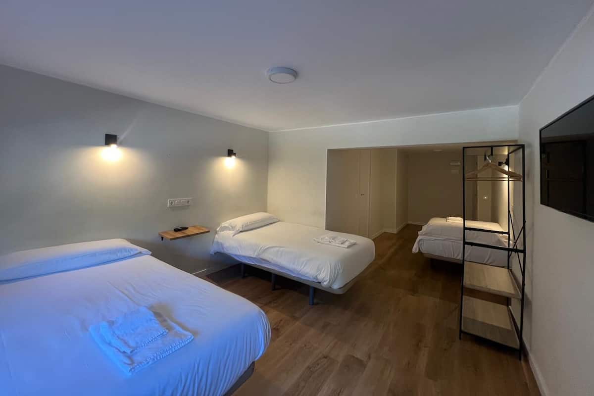 A modern hotel room with two single beds, a wardrobe, a mirror, and a small shelf with a remote control.