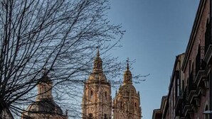 Una calle adoquinada con edificios históricos y una iglesia destacada con dos torres.