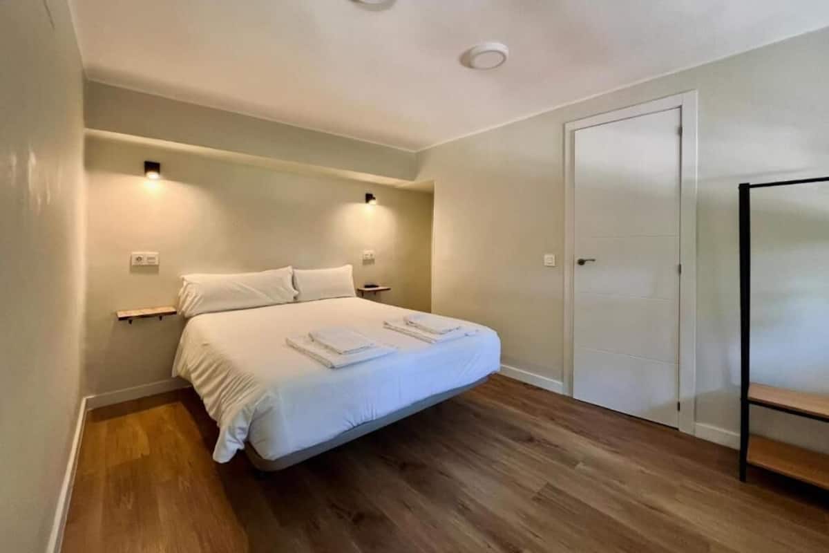 A bedroom with a bed, wooden flooring, a wardrobe, and two wall-mounted lights.