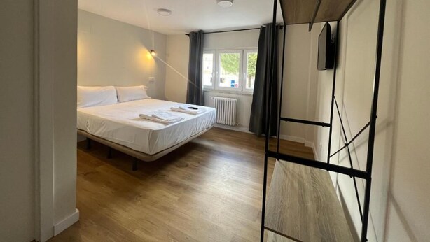Un dormitorio con cama, radiador, ventana con cortinas y televisor instalado en la pared.