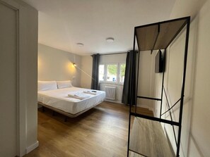 A bedroom with a bed, a radiator, a window with curtains, and a wall-mounted TV. - Hostal Mindanao (Salamanca)