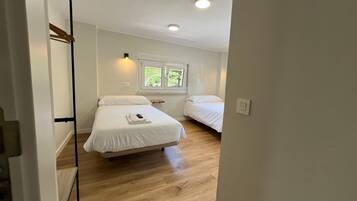 Un dormitorio con dos camas, una ventana y piso de madera.
