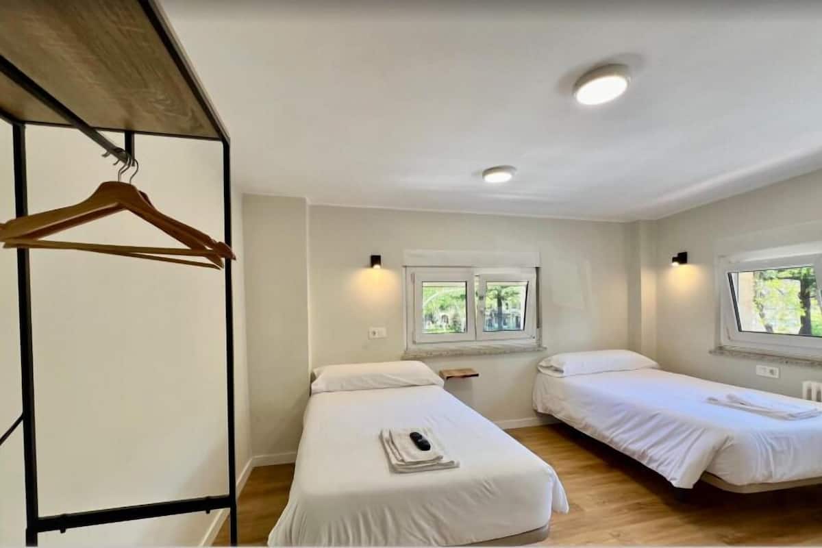 A hotel room with two single beds, a wooden hanger, a window with a view of greenery, and a ceiling light.