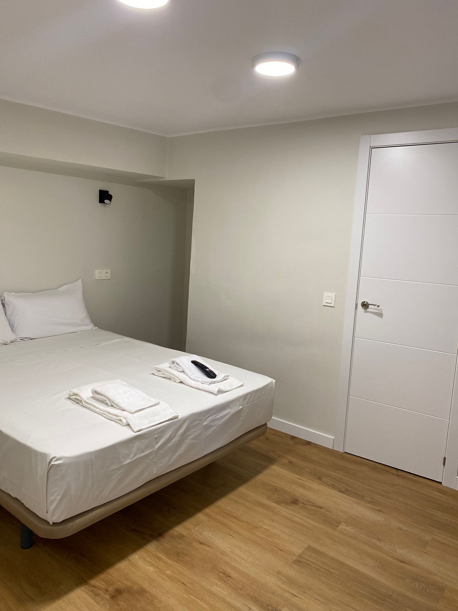 Una habitación de hotel con una cama individual, una mesita de noche, un control remoto y una puerta.