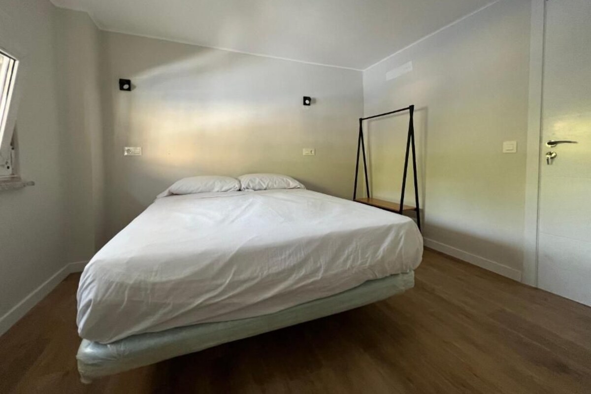 Un dormitorio con una cama, suelo de madera, una puerta blanca y un ventanal.