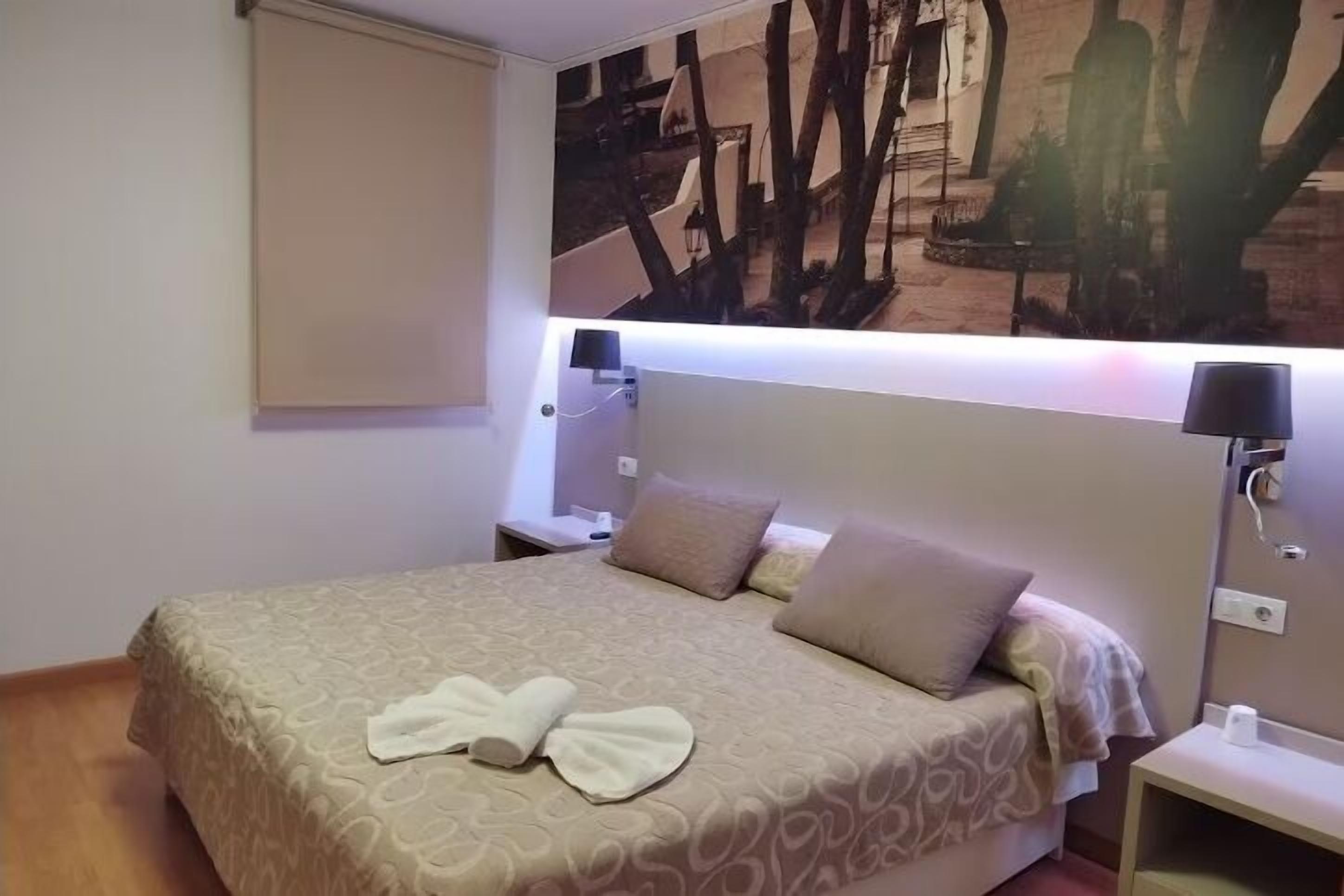 A hotel room with a bed, two bedside tables, a wall-mounted lamp, and a painting.