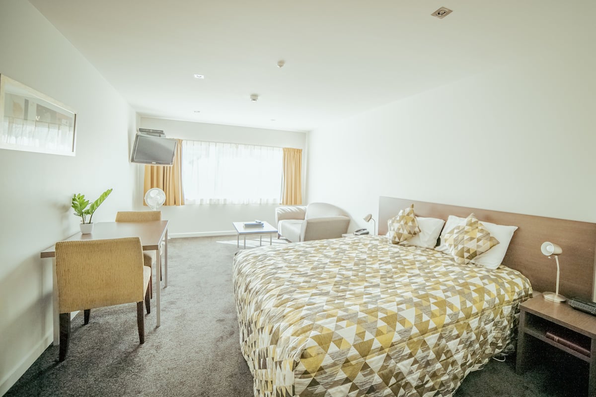 Une chambre d’hôtel avec un lit, un bureau, une chaise, une télévision et une fenêtre avec des rideaux.