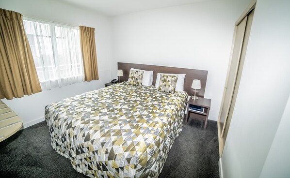 A hotel room with a large bed, a nightstand, a lamp, and a window with curtains.