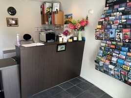 A reception desk with a clock, a small shelf with books and a vase of flowers, and a wall display of travel brochures.