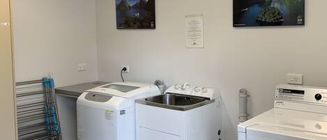 A laundry room with two front-loading washers and dryers, a drying rack, and two framed pictures on the wall.