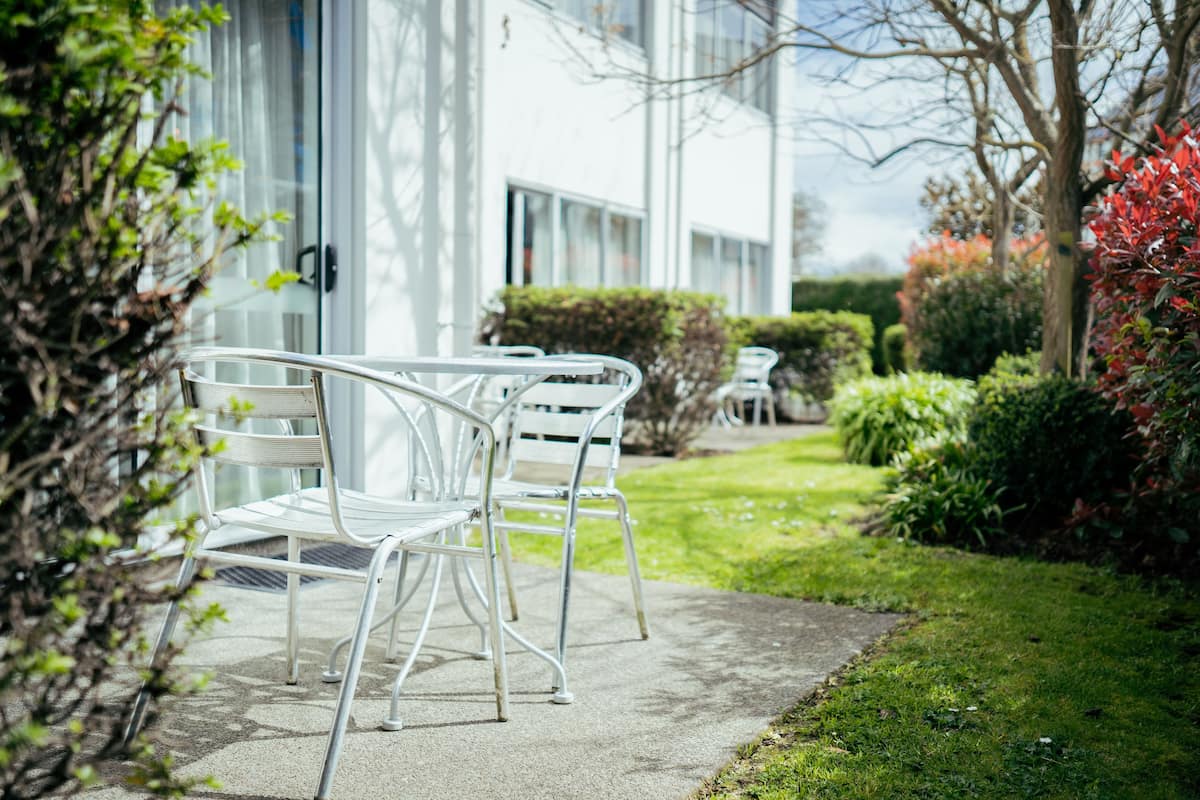 Un espace extérieur moderne aménagé avec des chaises et des tables en métal, une pelouse bien entretenue et un bâtiment aux grandes fenêtres en arrière-plan.