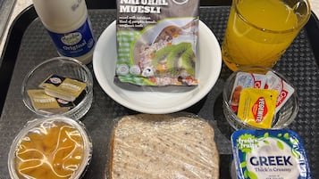 A breakfast tray with cereal, juice, yogurt, and a sandwich.