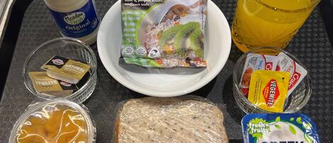 A breakfast tray with cereal, juice, yogurt, and a sandwich.