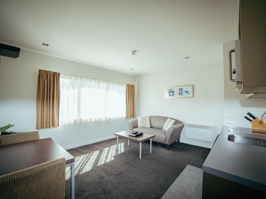 Una sala moderna con un sofá, una mesa de centro y un comedor con sillas. Cuenta con una cocina con un lavamanos y un televisor montado en la pared.