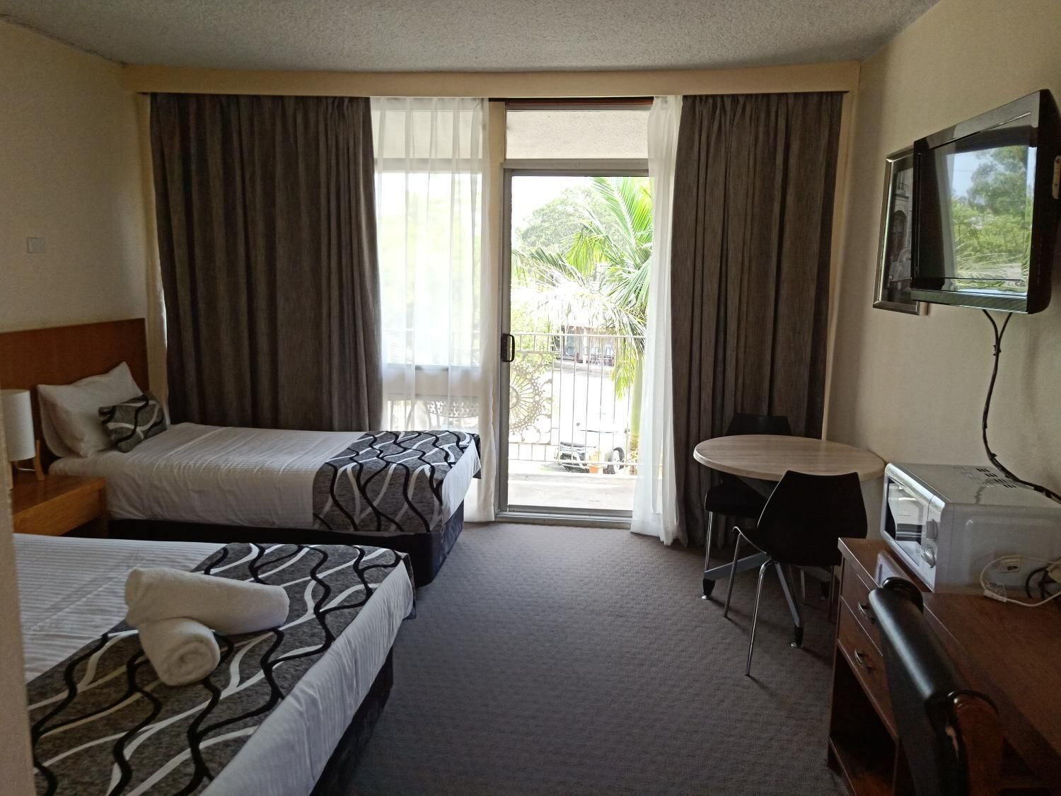 A hotel room with two beds, a desk, a chair, a television, and a view of the outdoors.