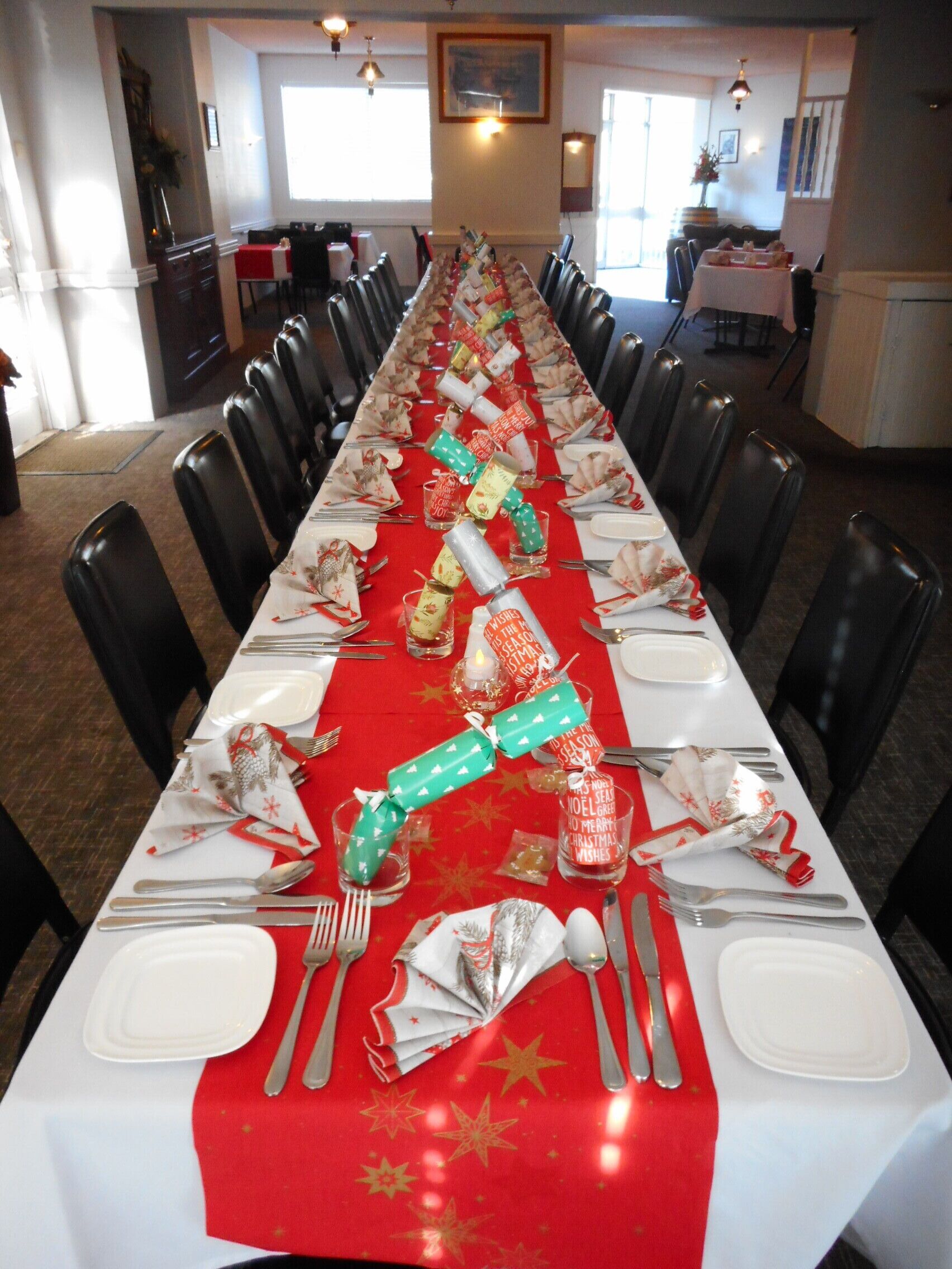 A long dining table set for a meal with a red tablecloth, white plates, silverware, and festive decorations.