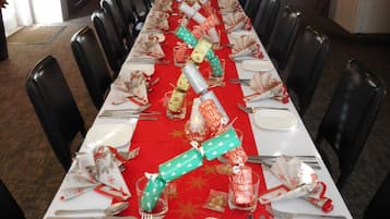 A long dining table set for a meal with a red tablecloth, white plates, silverware, and festive decorations.