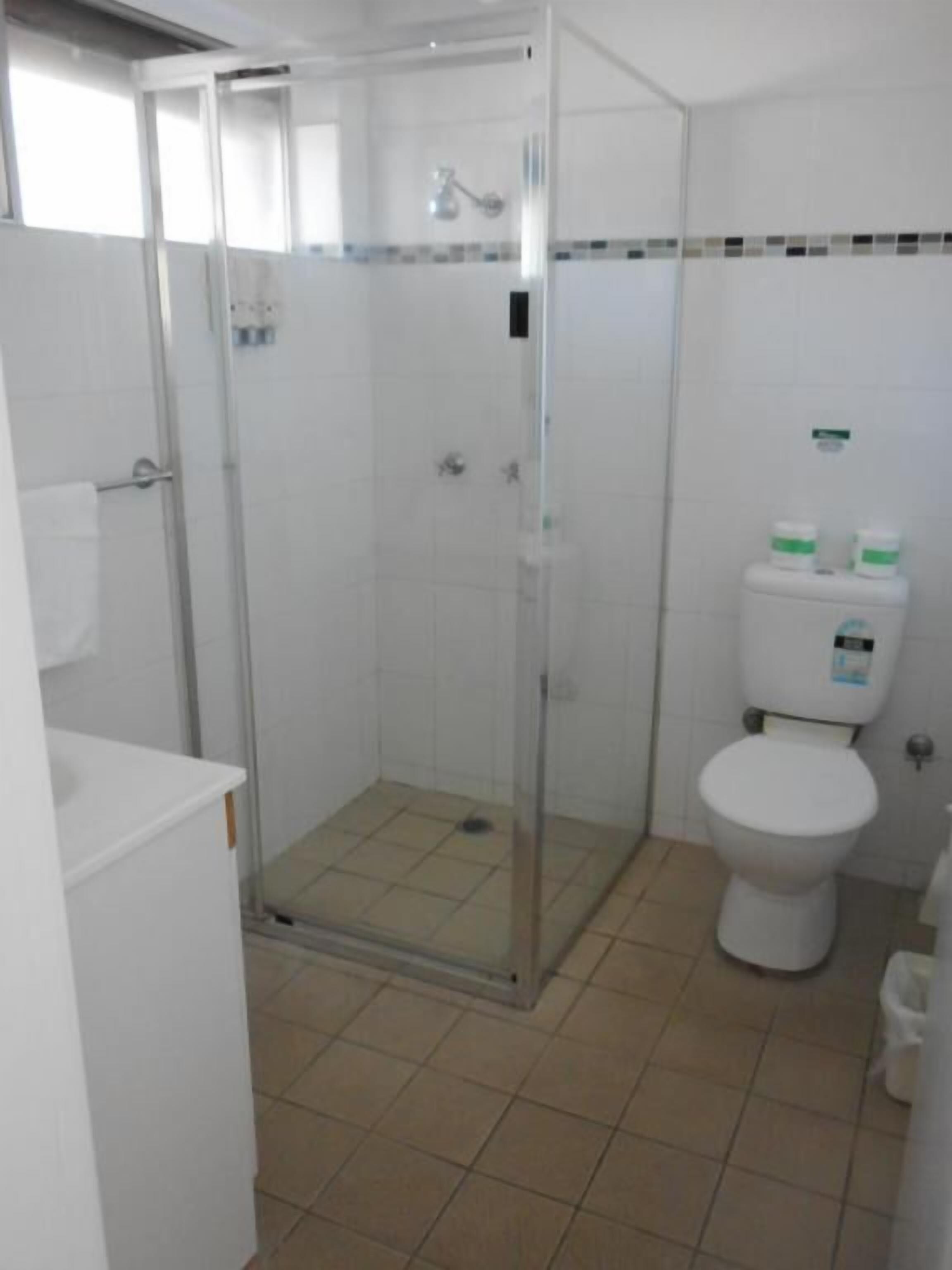 Un baño con ducha envuelta en vidrio, inodoro blanco y piso de baldosas.