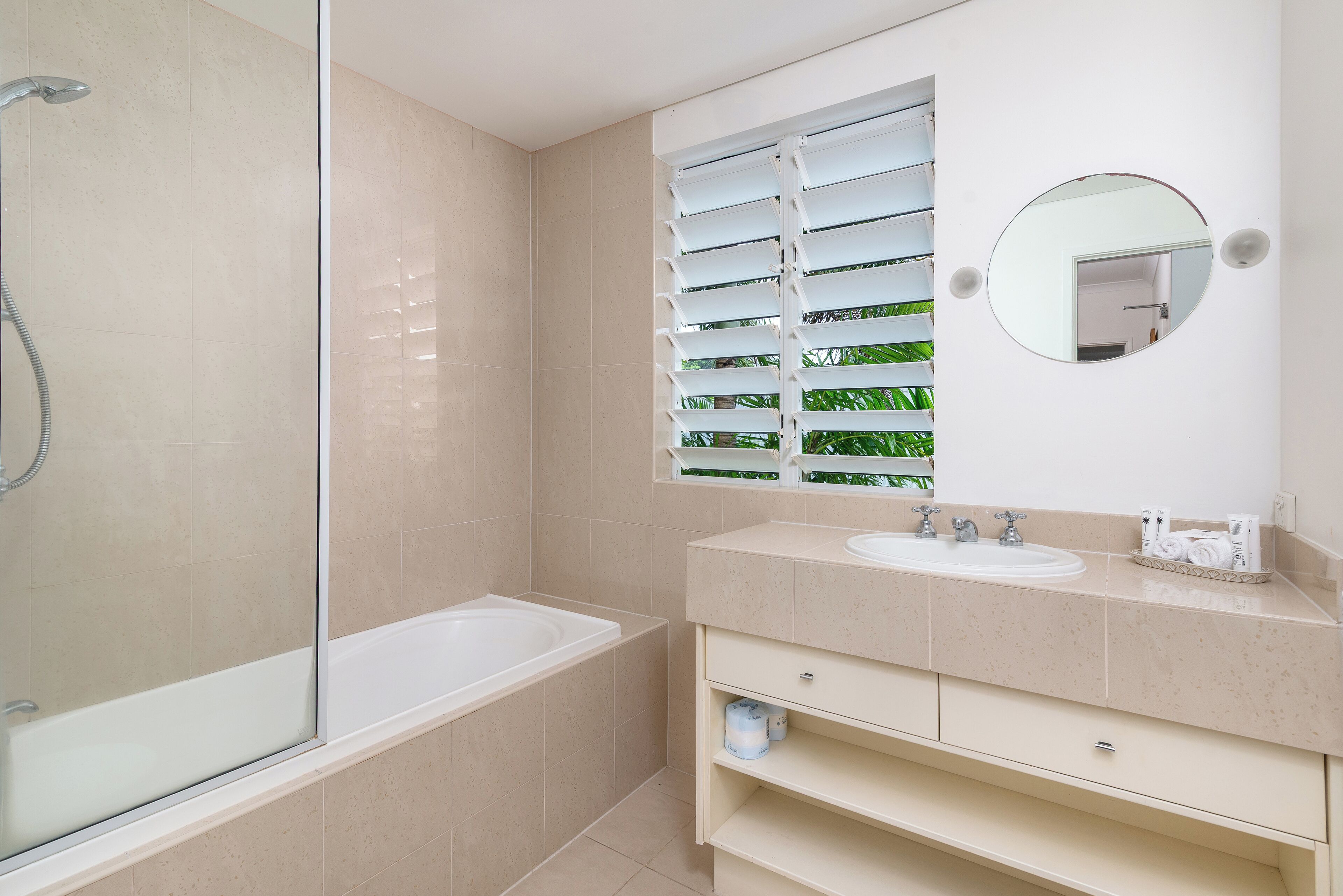 A modern bathroom with a glass-enclosed shower, a bathtub, a sink with a mirror, and a window with blinds.