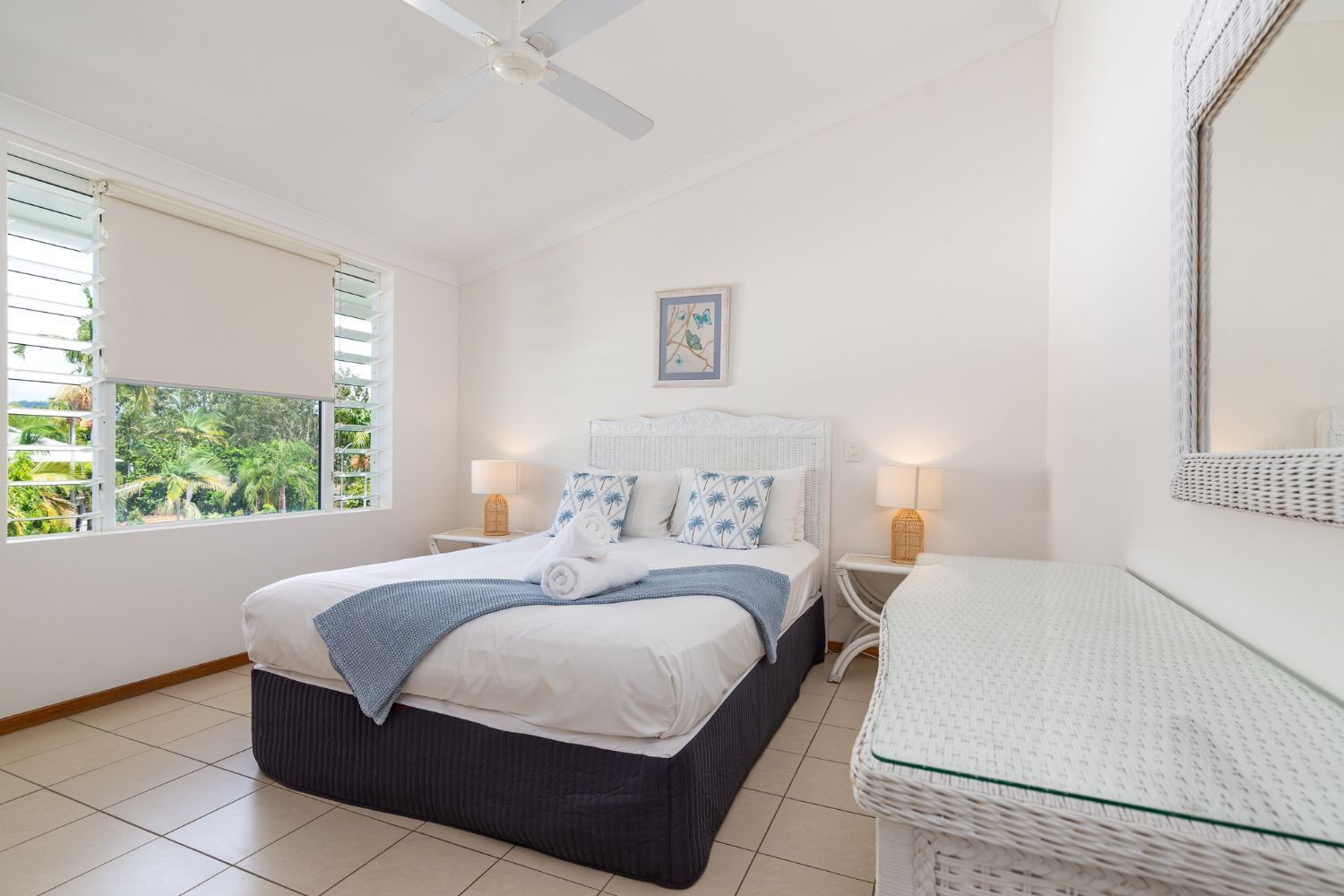 Makuuhuone, jossa on sänky, yöpöydät, kattotuuletin, ikkuna, josta on näkymä vehreään maisemaan, ja seinällä oleva kehystetty taulu.