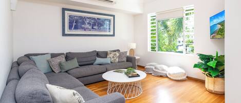 A modern living room with a grey sectional sofa, a round coffee table, and a large window with a view of greenery.