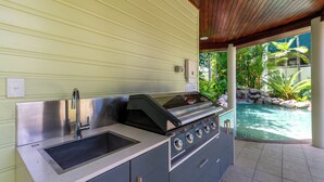 Et udendørs køkken med vask, grill og udsigt til en swimmingpool.