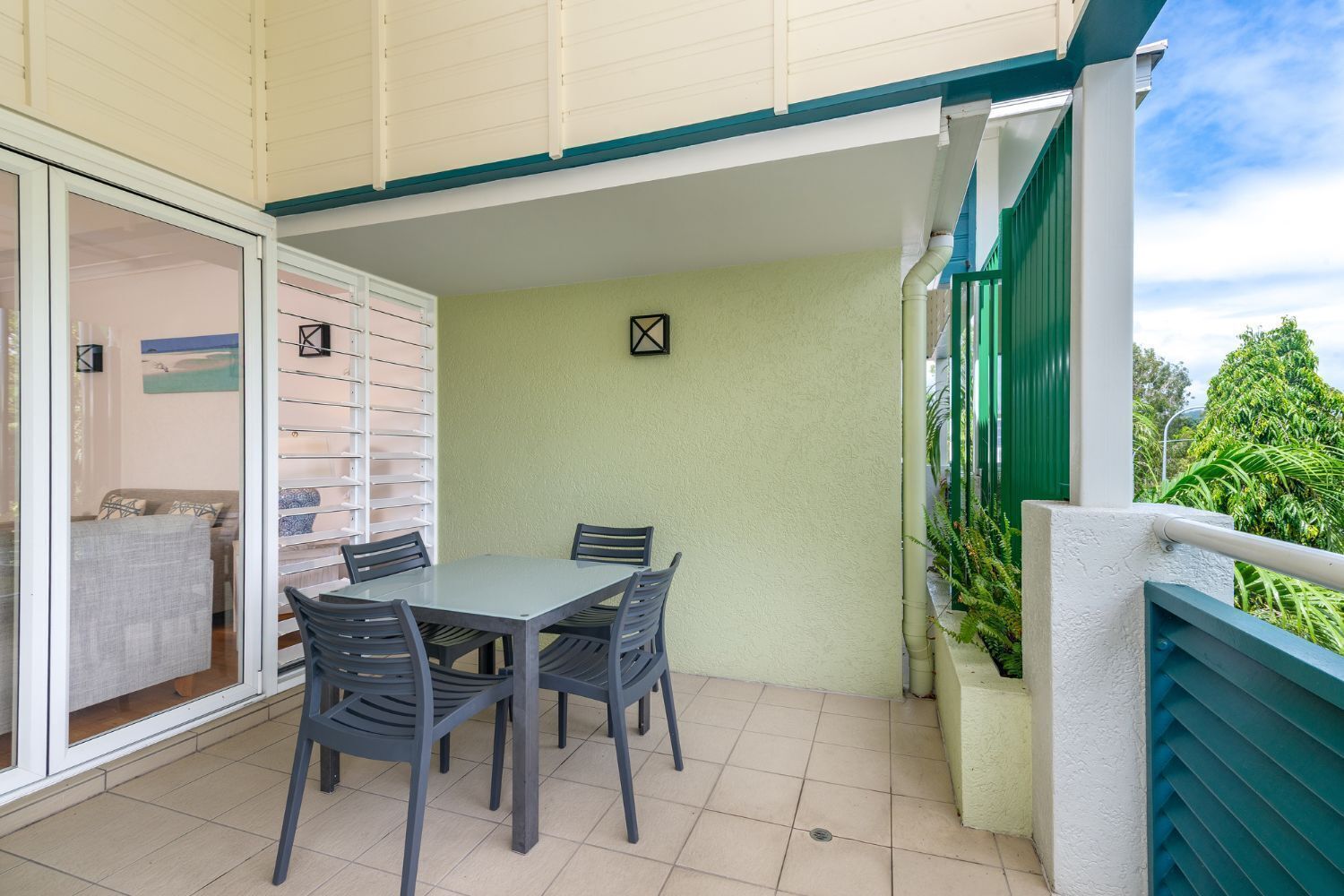 An outdoor patio with a table and chairs, a sliding glass door leading to an interior room, and a green railing.