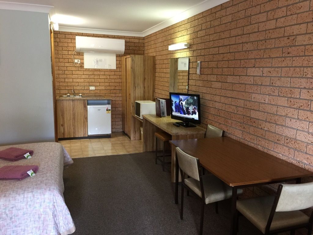 Quarto com cama, escrivaninha, televisão e uma pequena cozinha.