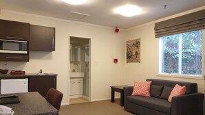 A compact living space with a kitchenette, a dining area, a sofa, and a window with blinds. - Eden Park Motel (Auckland)