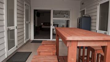 A wooden table and benches on a porch with a sliding glass door leading to a bedroom.