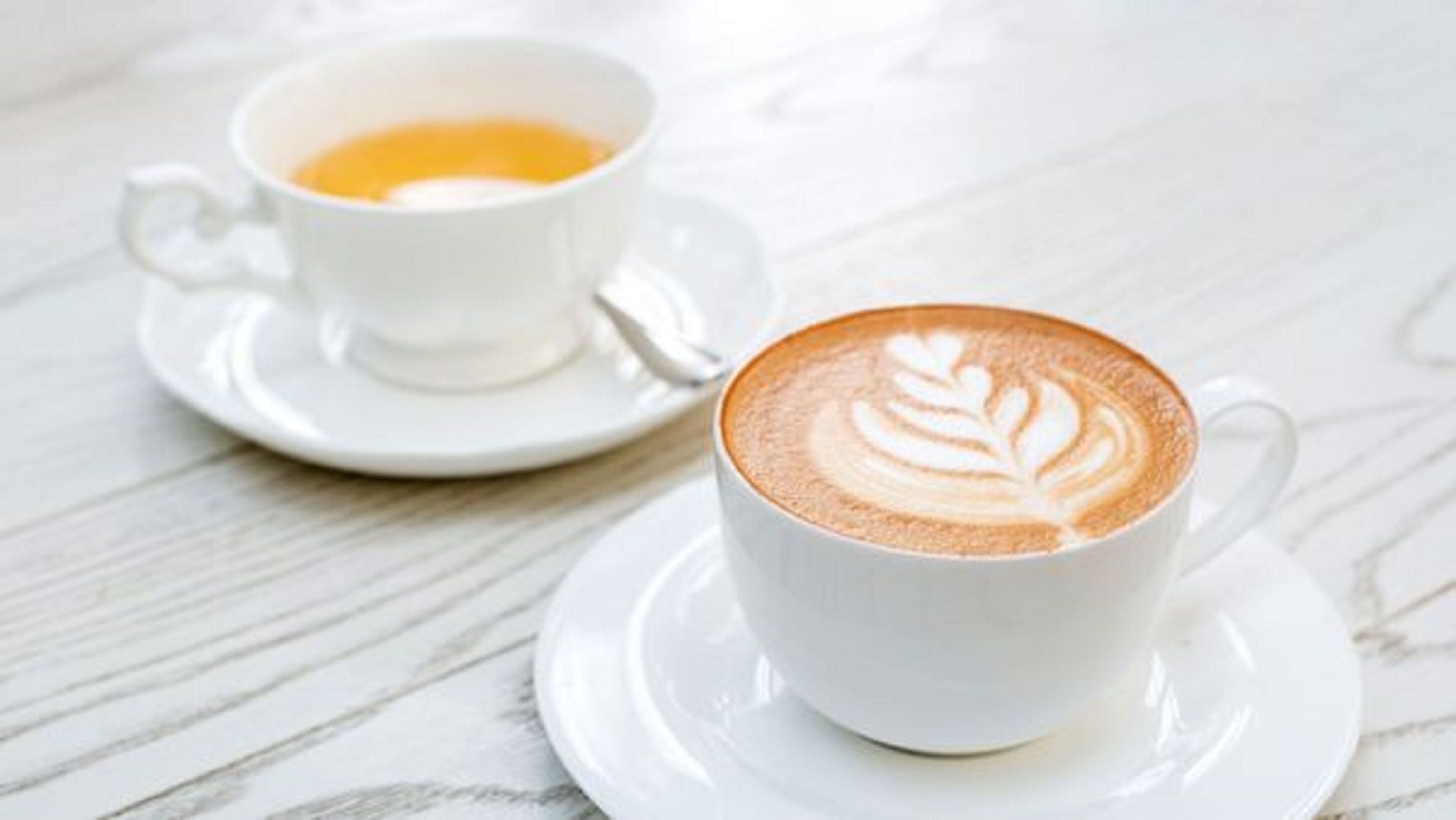 Twee witte koffiekopjes op een witte marmeren tafel.