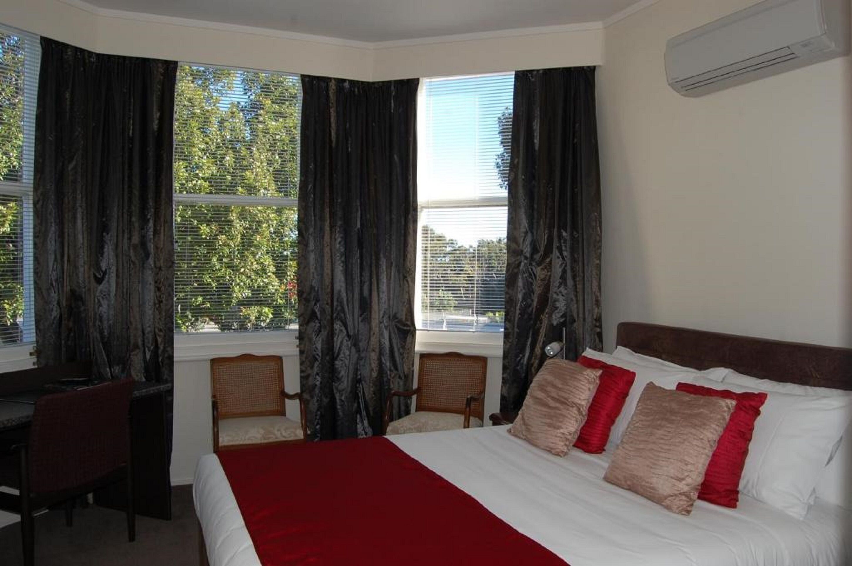 A hotel room with a large bed, a desk, two chairs, and a window with curtains.