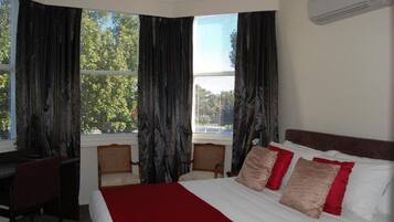 A hotel room with a large bed, a desk, two chairs, and a window with curtains.