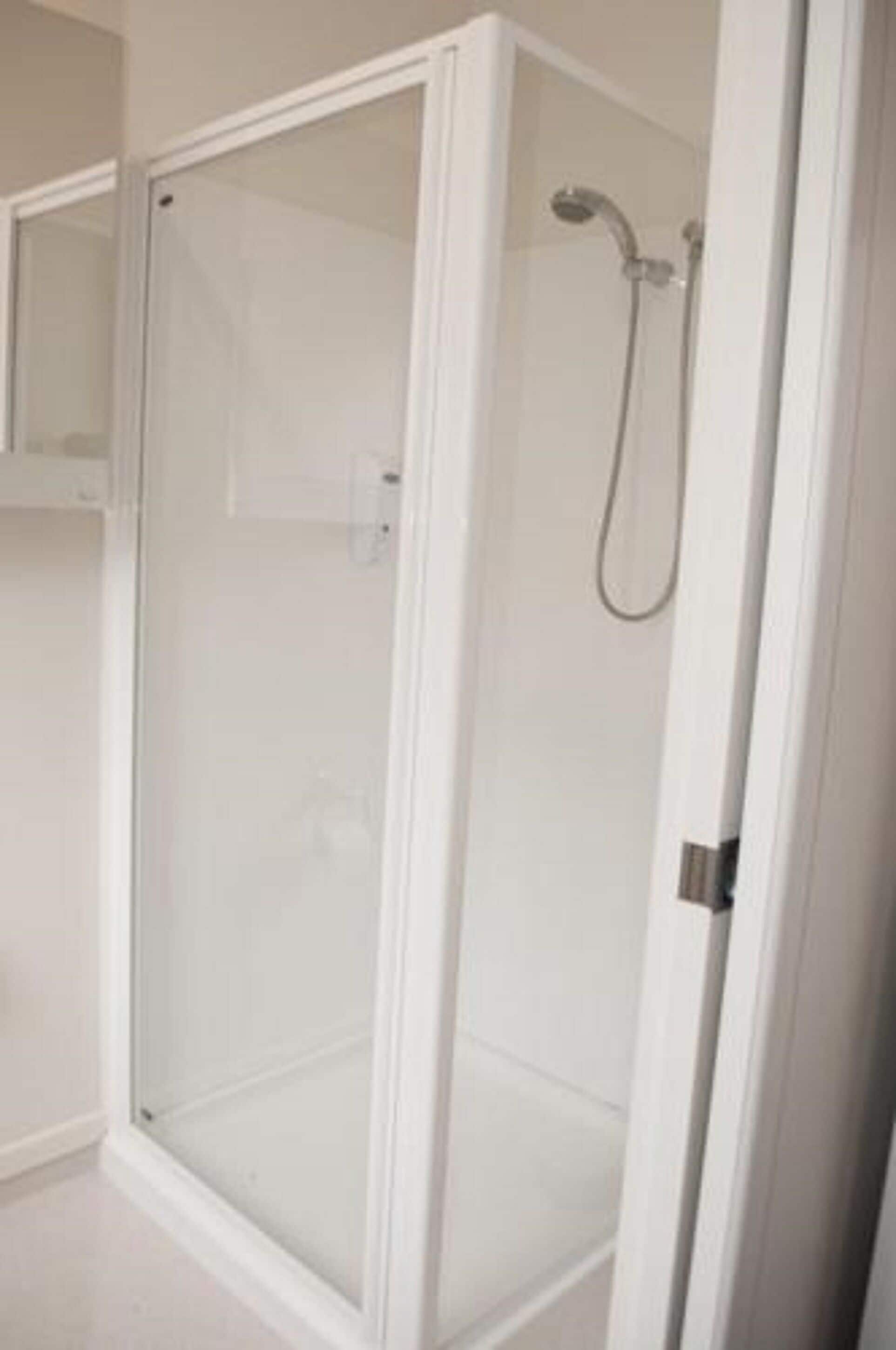 A white shower enclosure with a glass door and a showerhead.