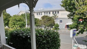 A covered outdoor area with a wooden table and chairs, a white railing, and a view of a building with a sign that reads "ENTRANCE". - Eden Park Motel (Auckland)