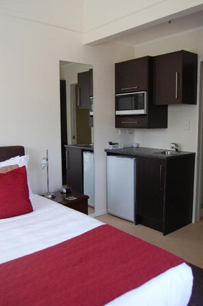A compact hotel room with a bed, a small kitchenette, and a mirror. - Eden Park Motel (Auckland)