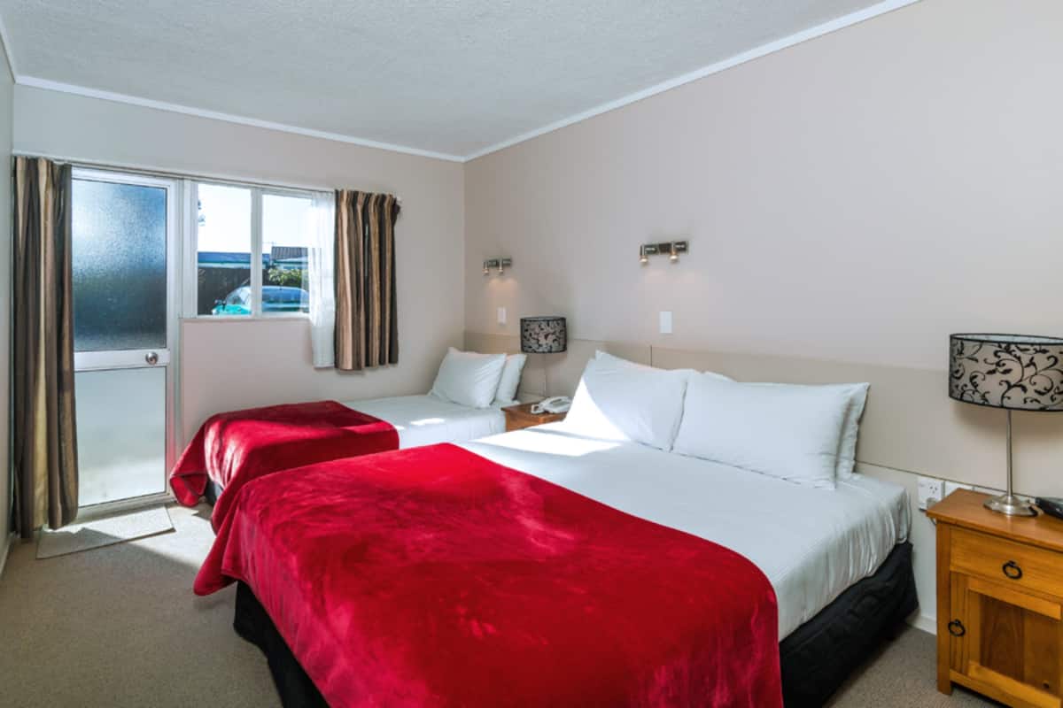 A hotel room with two beds, a sliding glass door, a wooden nightstand, and a lamp.