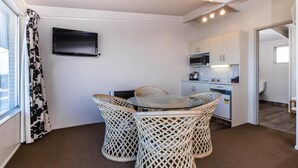 A room with a glass-top table surrounded by wicker chairs, a flat-screen TV mounted on the wall, and a kitchenette with a microwave and stove. - Twin Peaks Lakeside Inn (Taupo)