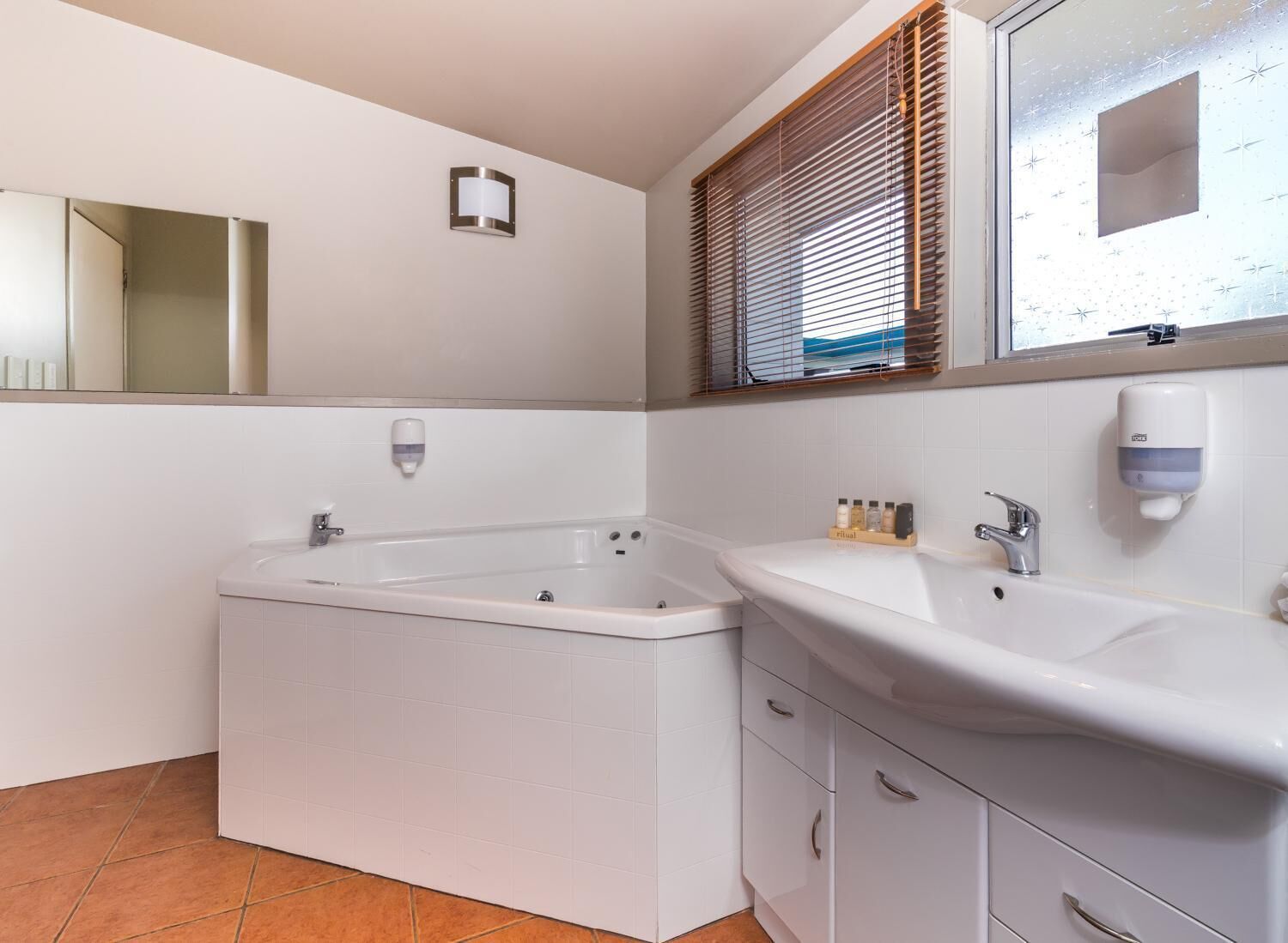 A bathroom with a bathtub, a sink, a mirror, and a window with blinds.