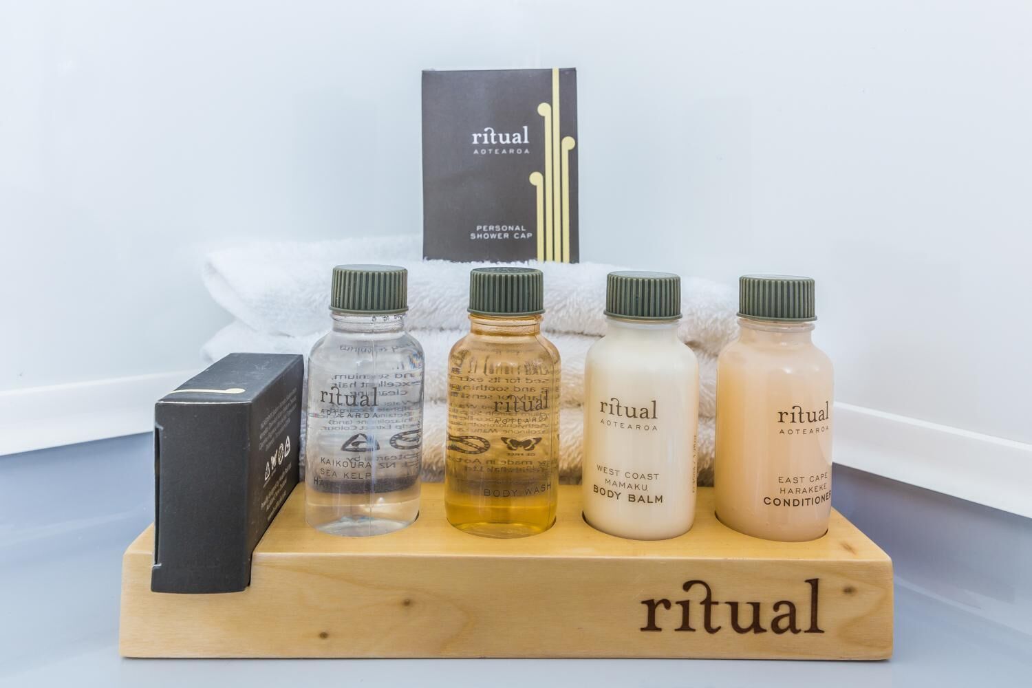A wooden display stand with five bottles of Ritual Aotearoa personal care products, including body wash, body balm, and conditioner, along with a black box.