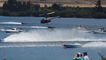 Un helicóptero volando sobre un lago con barcos y gente en la orilla.