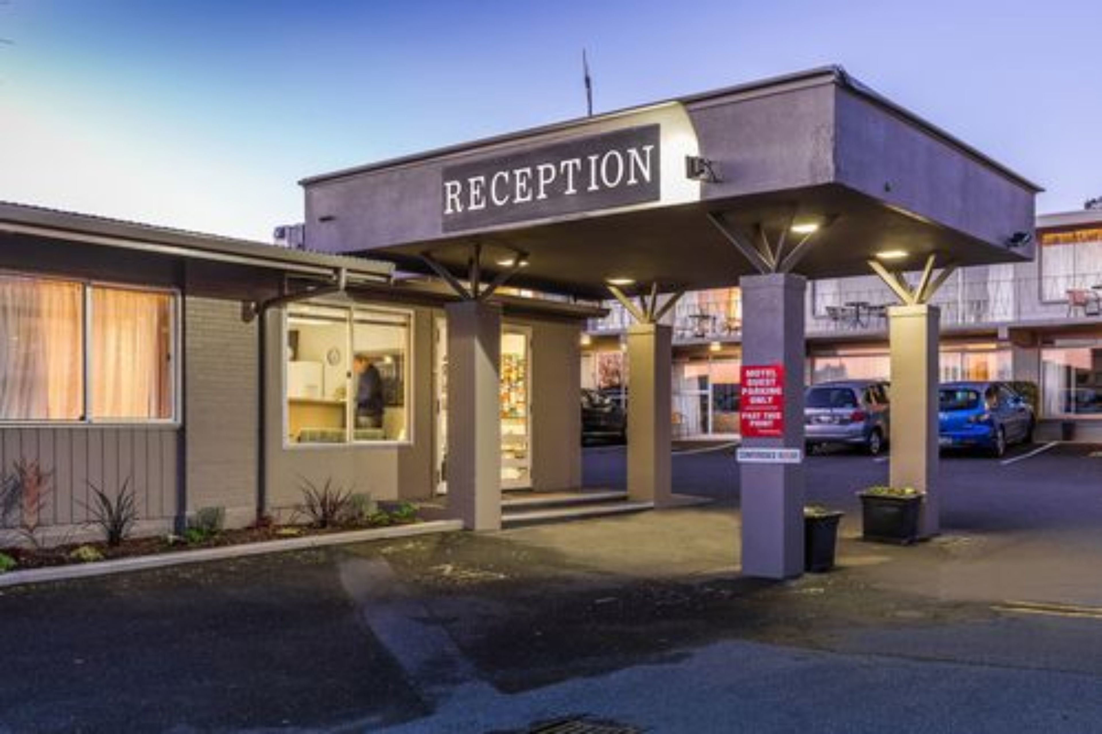 Ett receptionsområde med en skylt, en överbyggd entré och en parkeringsplats med bilar.