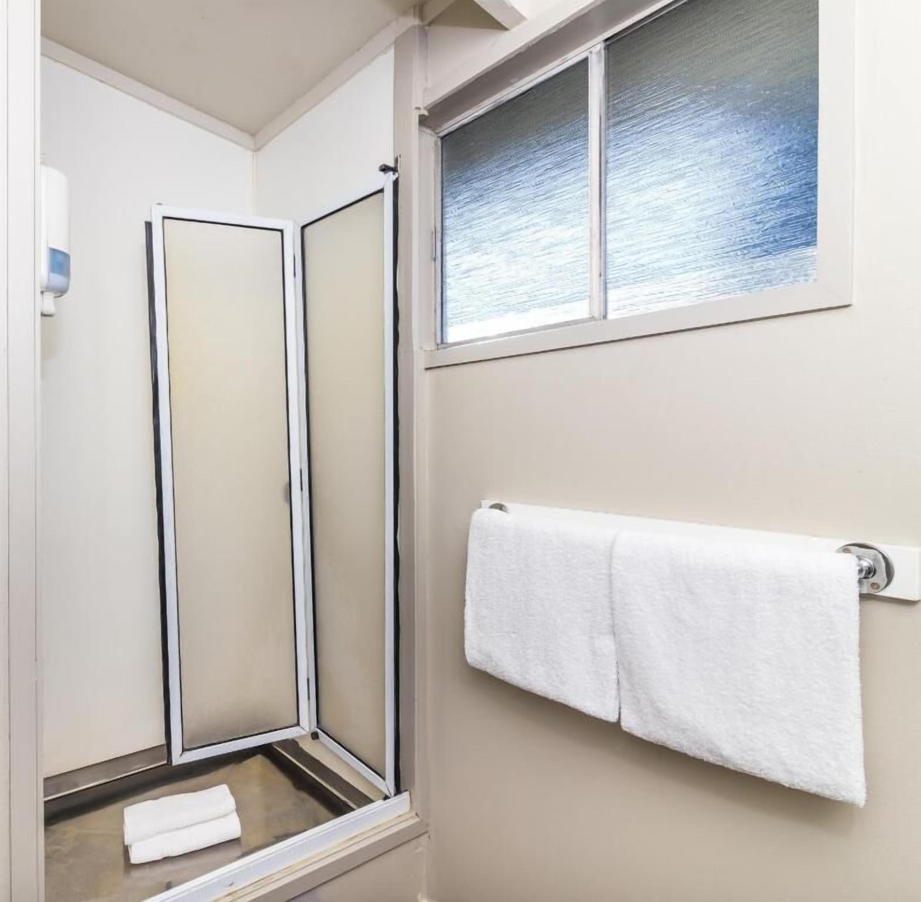 Een badkamer met een douche, een raam met uitzicht en een handdoekhouder met twee handdoeken.